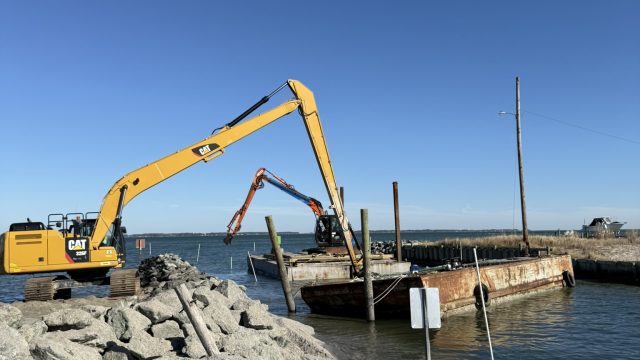 Early Marine Construction excavators and barge working on a stone jetty at the water's edge