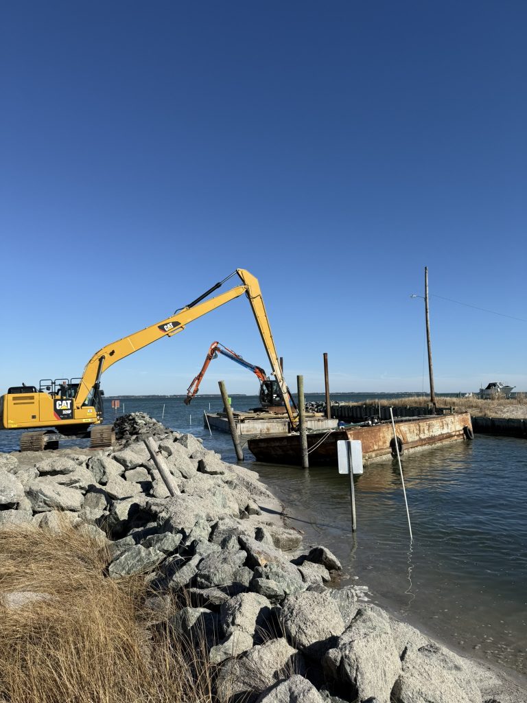 Early Marine Construction excavators and barge working on a stone jetty at the water's edge